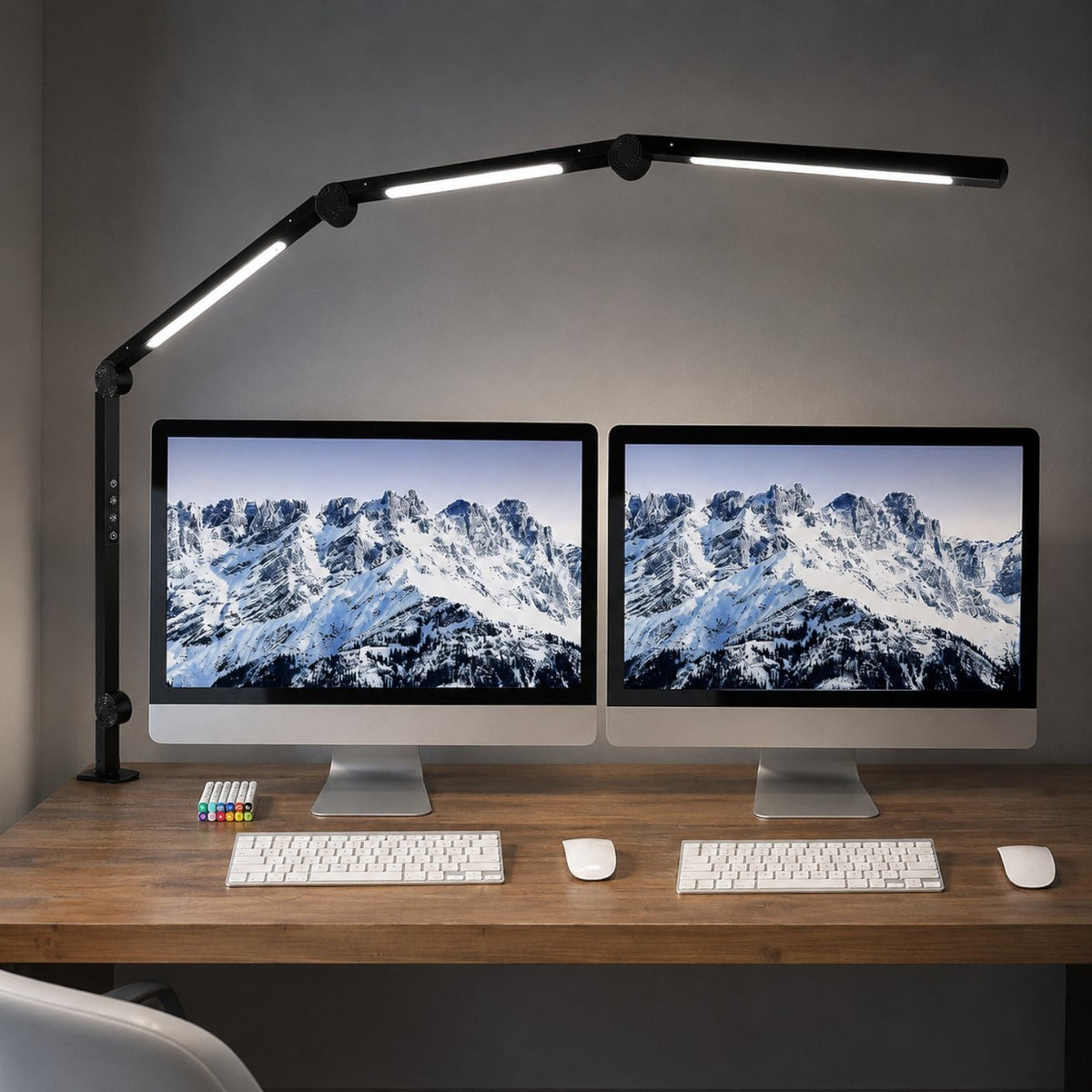 Black Melora LED desk lamp with swing arm, clamped to a desk with dual monitors